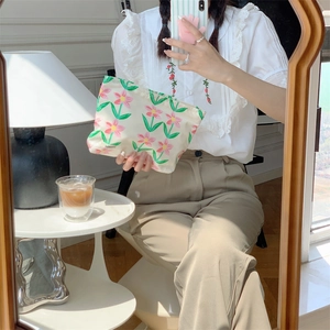 Detail of floral cotton makeup bag reflected in mirror held by hands in warm interior