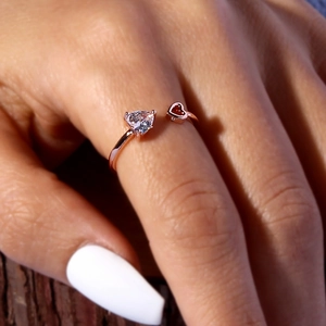 Macro shot of rose gold open ring featuring large clear and small red heart stones