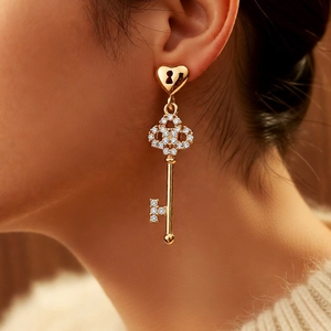 Detail of 18k gold plated heart ear stud with rhinestone key pendant on a model