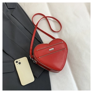 Macro detail of red heart-shaped shoulder bag featuring glossy finish and silver zippers