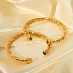 Detailed shot of golden twist cable bangles with blue and amber stones on silk background