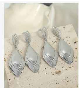 Macro shot of silver diamond-shaped wavy earrings with small rhinestones on stone background