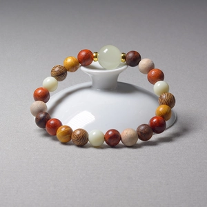 Multi-material Buddhist bead bracelet with wood and jade beads on a white ceramic plate