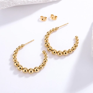Detailed view of C-shaped gold beaded hoop earrings with butterfly backings and high polish