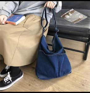 Detail of large denim hobo bag featuring an adjustable strap and a deep blue front pocket
