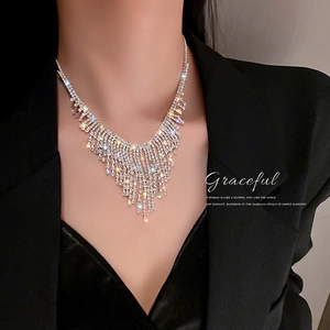 Elegant silver tassel necklace with rhinestones worn by a model on a dark suit background