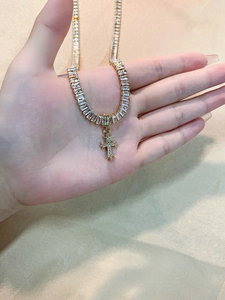 Detail of gold tennis chain necklace with sparkling zircon cross pendant held in hand