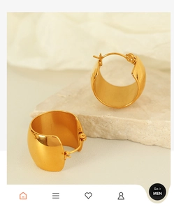 Close-up of golden wide-hoop earrings on a beige stone and soft fabric background