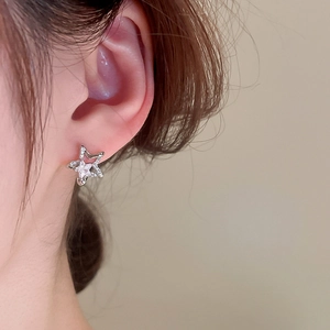 Macro close-up showing a silver star-shaped stud earring with zircon on a person ear