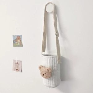 Close-up of quilted cup bag featuring embroidered plush bear and woven shoulder strap
