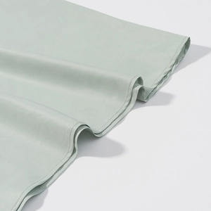 Detailed close-up of smooth satin fabric hem with precise stitching on light green dress