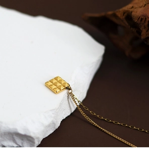 Detailed macro view of a gold square chocolate pendant on an asymmetric chain