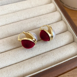 Close-up of golden spherical earrings with red flocking and white pearl in a beige box