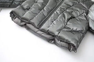 Macro shot of dark grey metallic puffer jacket hem with zipper and drawstring details
