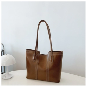 Close-up of deep brown leather tote bag with white contrast stitching on a minimalist table