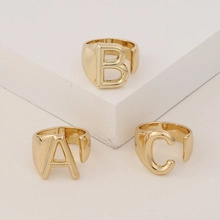 Detailed view of three 18K gold letter rings A B and C on white geometric blocks
