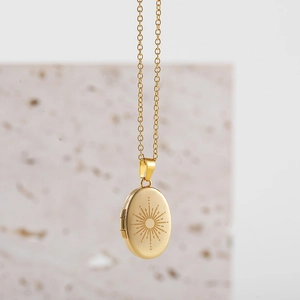 Detail of a gold oval locket necklace with sunburst engraving and side hinge for photos