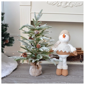 Miniature flocked Christmas tree with warm LED lights and snowman doll near fireplace