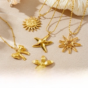 Detailed view of gold plated necklaces with starfish, sun, and bow pendants on sand
