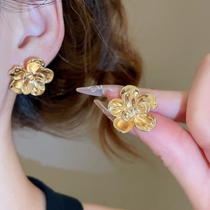 Detail showing the size and high-polished texture of golden flower stud earrings