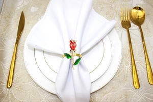Close-up of golden red rose napkin ring with rhinestones on a white fabric napkin