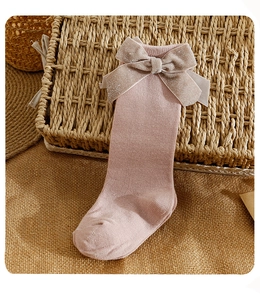 Detailed knit texture of pink kids high socks with sparkling velvet bow decoration