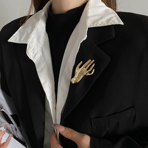 Close-up of polished gold hand-shaped brooch pinned on a black and white suit lapel