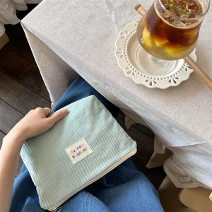 Close-up of a mint green corduroy pouch held by a model in a cozy cafe setting