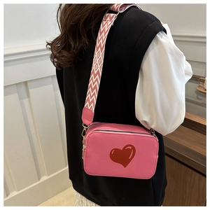 Pink crossbody bag with red heart detail and decorative patterned wide shoulder strap