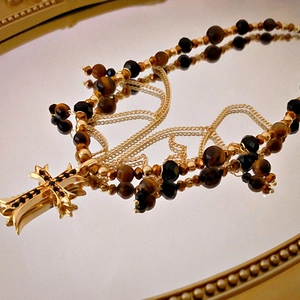 Detail of tiger eye beaded necklace with a golden gothic cross pendant and black stones