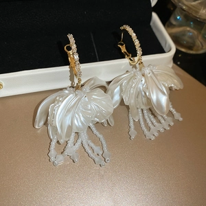 Macro detail of elegant white floral tassel earrings with golden accents on a jewelry box