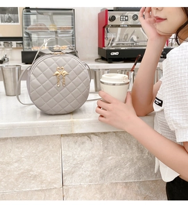 Close-up of a grey round crossbody bag with quilted rhombic pattern and flamingo charm