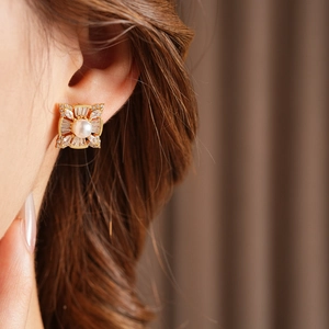 Close-up of golden square stud earring with a central pearl and sparkling zircon stones