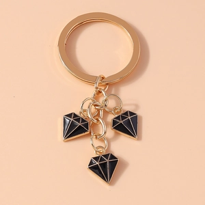 Detail view of stylish golden keychain with three black enamel diamond pendants on beige base