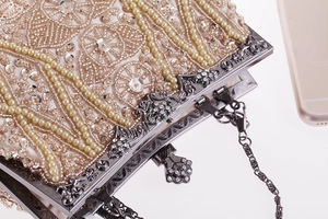 Dettaglio macro di pochette beige con ricami di perle, paillettes e catena in argento