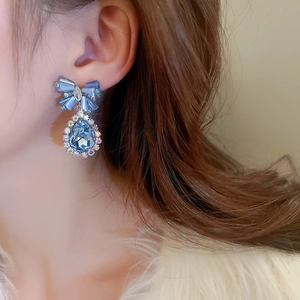 Macro detail of elegant blue crystal bow with teardrop drop earring worn on ear