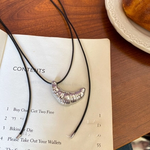 Minimalist croissant pendant necklace with black leather cord over an open book