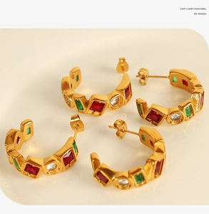 Detail of C-shaped 18K gold plated earrings with red and green gemstone inlays