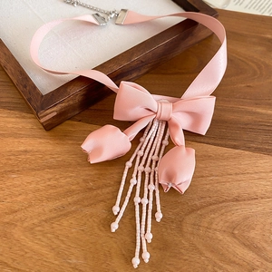 Detail of pink fabric bow necklace featuring beaded tassels on a white display tray