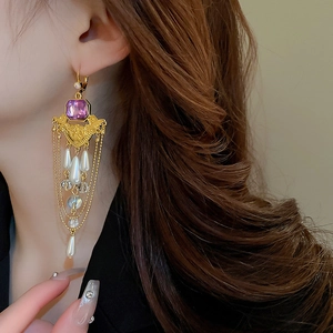 Détail de boucles d'oreilles dorées avec pampilles, gemme violette et perles blanches