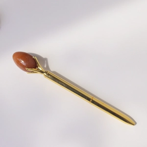 Macro detail of golden metal ballpoint pen featuring a claw-set red quartz gemstone egg