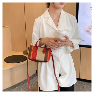 Detail of a striped canvas crossbody bag with red leather handles in a stylish cafe setting