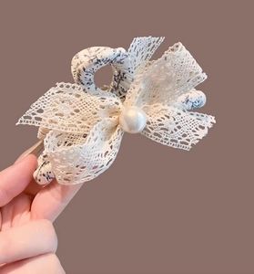 Détail de la pince à cheveux en dentelle florale avec nœud bleu et perle blanche