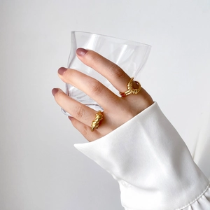 Detailed view of gold twisted rope rings worn on hand while holding a clear glass