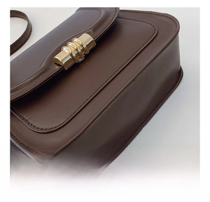 Close-up of brown leather saddle bag showing precise stitching and gold metal lock detail