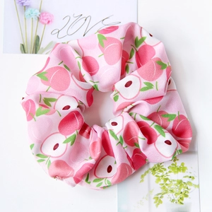 Detail of pink fabric scrunchie with peach and apple patterns on white background
