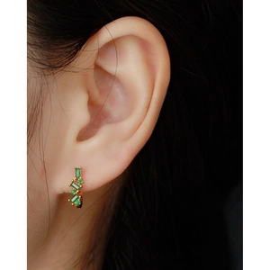 Close-up of a U-shaped gold earring featuring vertical green zircons on a model's ear