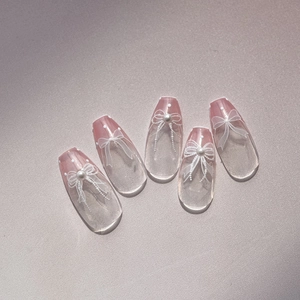 Detail of transparent nail stickers featuring white bows and pearl accents