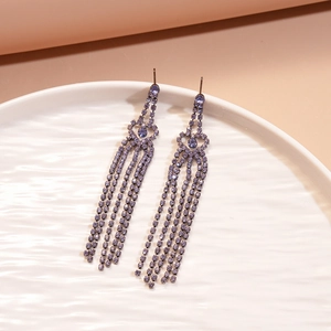 Close-up of elegant purple tassel earrings with crystals on a white ceramic plate