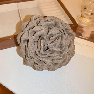 Close-up of a camel fabric flower hair claw clip on a white table with natural lighting